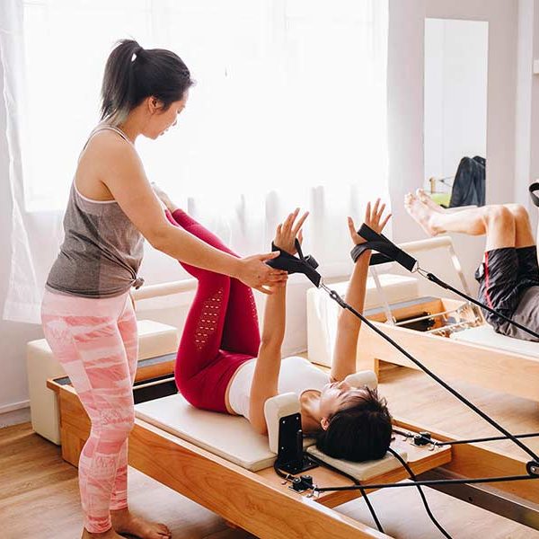 Pilates Instructor Teaching a Student Hands in Straps on the Reformer